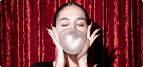 Person blowing bubble gum against a red curtain